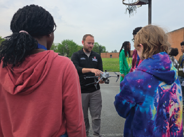 man holding drone while students observe